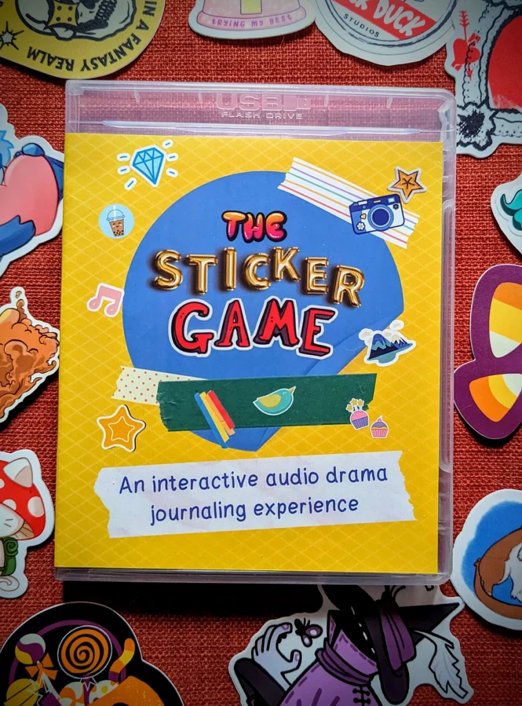 A physical copy of The Sticker Game: An interactive audio drama journaling experience surrounded by an array of stickers on an orange fabric background.